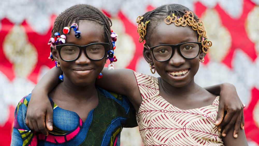 Zwei hübsche afrikanische Schülerinnen freuen sich über ihre neuen Brillen und umarmen sich.