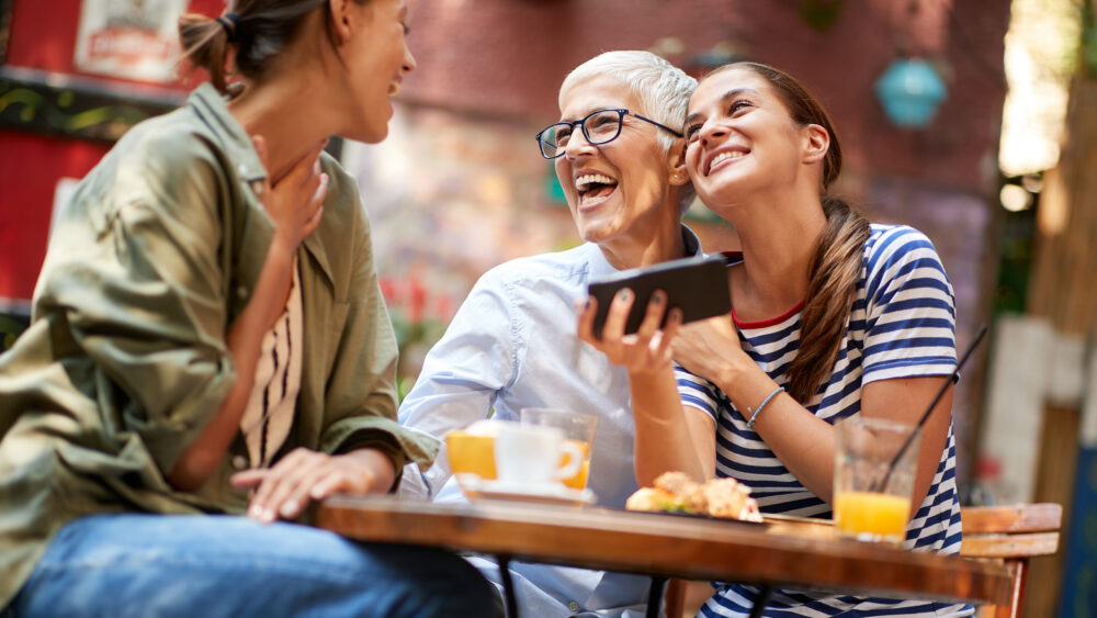 Eine Gruppe von Freundinnen verschiedener Generationen lacht zusammen im Café.